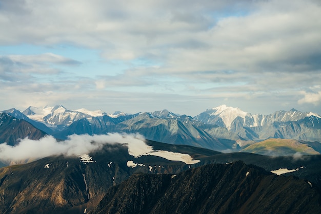 Atmosphärische Alpenlandschaft mit großen, goldglänzenden, schneebedeckten Felsen und einem riesigen Gletscher in der goldenen Stunde. Niedrige Wolken auf Schneeberg im Sonnenaufgang. Über Berge über Wolken fliegen. Wunderbare Hochlandlandschaft.