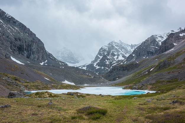 Foto atmosphärische berglandschaft mit gefrorenem alpensee und hohen verschneiten bergen tolle bewölkte landschaft mit eisigem bergsee auf dem hintergrund von schneeberg in niedrigen wolken schöner blick auf den eissee