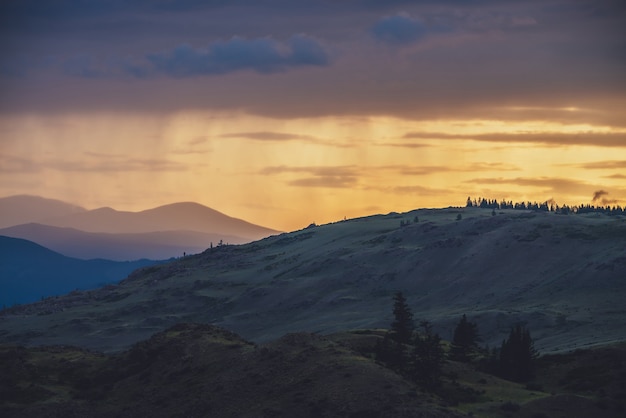 Atmosphärische Landschaft mit Silhouetten von Bergen mit Bäumen auf dem Hintergrund des lebendigen orange-blau-violetten Morgenhimmels. Bunte Naturlandschaft mit Sonnenuntergang oder Sonnenaufgang in leuchtender Farbe. Sundown Paysage