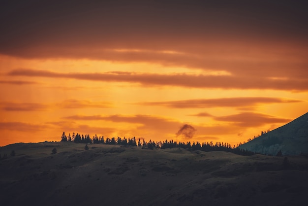 Atmosphärische Landschaft mit Waldsilhouette auf der Silhouette des Berges auf dem Hintergrund des lebendigen orangefarbenen Morgenhimmels. Bunte Naturlandschaft mit Sonnenuntergang oder Sonnenaufgang in leuchtender Farbe. Sundown Paysage.