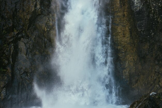 Atmosphärische minimale Landschaft mit vertikalem großen Wasserfall an der Felswand. Mächtiger großer Wasserfall in dunkler Schlucht. Naturhintergrund des hohen vertikalen turbulenten fallenden Wasserstroms auf nassen Felsen