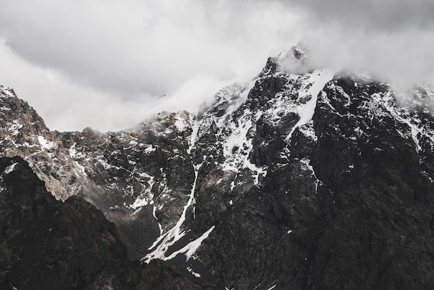 Atmosphärische minimalistische Alpenlandschaft mit schneebedecktem felsigem Berggipfel