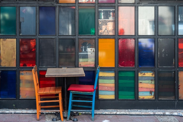 Atmosphärische Sommerfotografie Caféstühle aus Holz auf dem Tisch vor dem Hintergrund bunter Gläser offenes Straßencafé