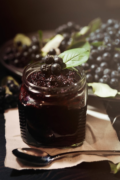 Atolamento de chokeberries pretos (aronia melanocarpa) e seus frutos na mesa escura. conservas caseiras.