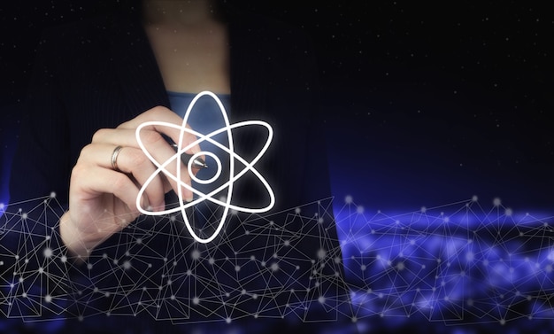 Atom-Molekül-Zusammenfassung. Hand, die digitalen Grafikstift hält und digitales Hologramm-Molekül-Atomzeichen auf dunklem, unscharfem Hintergrund der Stadt zeichnet. Atommolekül als Konzept für die Wissenschaft.