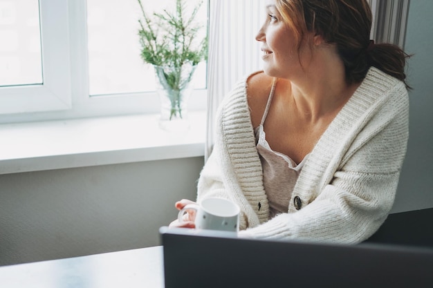 Atractiva y amable mujer morena sonriente de mediana edad usando una laptop en casa vibraciones acogedoras temporada de invierno