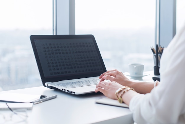 Foto atractiva asistente femenina trabajando, escribiendo, usando una computadora portátil, concentrada