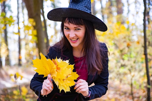 Atractiva bruja en el bosque de otoño evoca hojas de arce caídas amarillas en el fondo