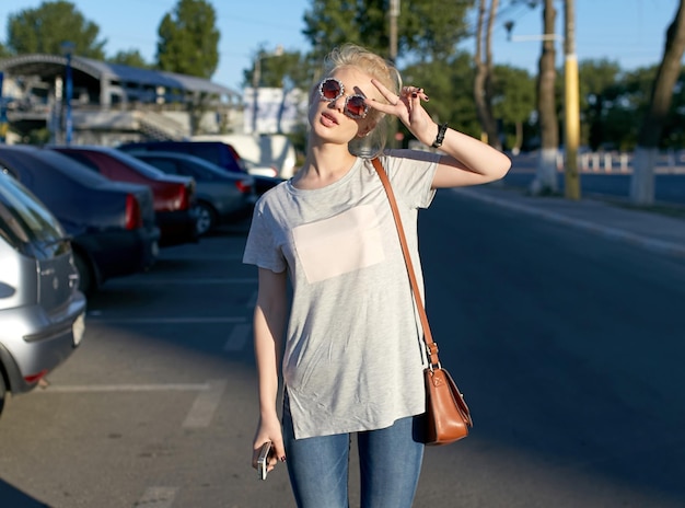 Atractiva chica alegre caminando en la ciudad urbana usa gafas de sol mostrar vsign