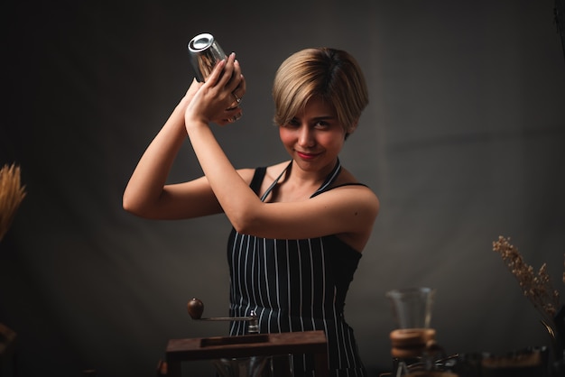 Atractiva chica bartender sosteniendo en sus manos cocteleras de acero en la barra del bar