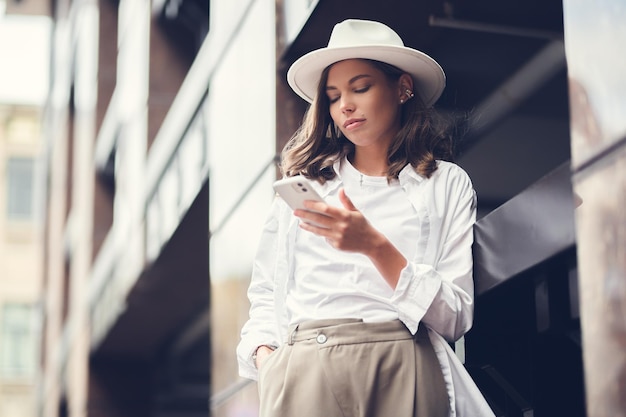 Atractiva chica caucásica blanca con elegante ropa blanca y sombrero blanco con un teléfono móvil