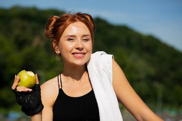 Foto atractiva chica caucásica pelirroja comiendo manzana después del entrenamiento deportivo. espacio para texto