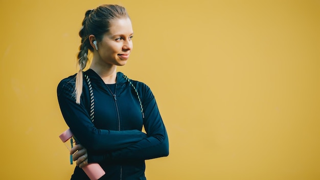 Atractiva chica caucásica sobre fondo amarillo aislado con auriculares inalámbricos en traje deportivo hacer ejercicio correr y beber agua