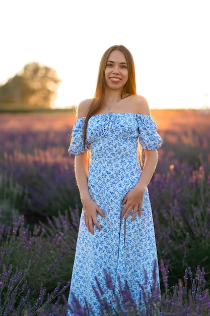 Atractiva chica delgada y feliz con un vestido azul en un campo de lavanda al atardecer