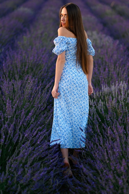 Atractiva chica delgada y feliz con un vestido azul en un campo de lavanda al atardecer