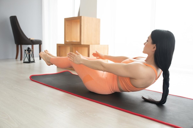 Atractiva chica delgada en ropa deportiva está haciendo ejercicios abdominales en el suelo en casa