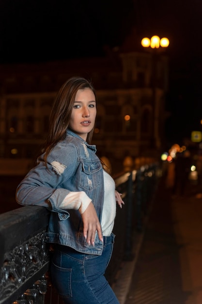 Atractiva chica con estilo en la calle de la ciudad de noche Retrato de mujer joven en chaqueta de mezclilla en el fondo de la ciudad de noche
