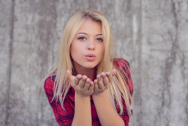 Atractiva chica feliz con cabello rubio, labios grandes, con piel perfecta y maquillaje enviando beso al aire. Ella está mirando a puerta cerrada, cara sonriente