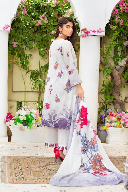 Atractiva chica joven en pose trasera con un vestido floral blanco para una sesión de moda al aire libre