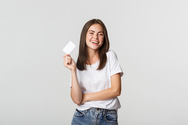 Atractiva chica morena feliz riendo y sosteniendo la tarjeta de crédito, blanco.