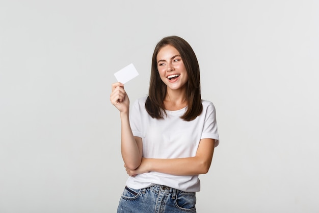 Foto atractiva chica morena feliz riendo y sosteniendo la tarjeta de crédito, blanco.