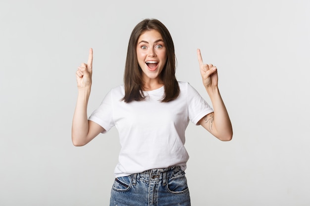 Atractiva chica morena sonriente apuntando con el dedo hacia arriba