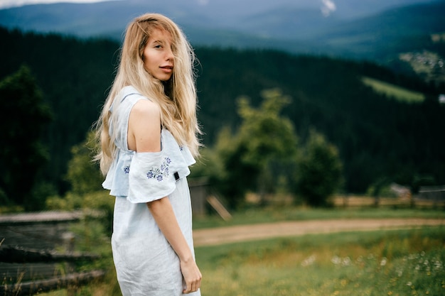 Atractiva chica rubia elegante joven en vestido romántico azul posando sobre un paisaje pintoresco