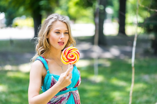 Atractiva chica rubia con un lollipop en el parque en verano