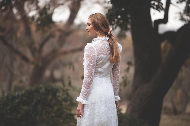 Atractiva chica rubia con vestido blanco vintage caminando en el bosque