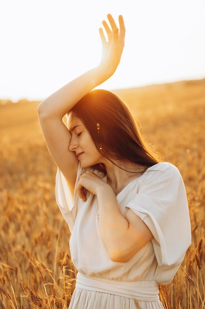 Atractiva chica ucraniana con cabello largo oscuro, esbelta y hermosa posando para una foto en un campo amarillo soleado con trigo