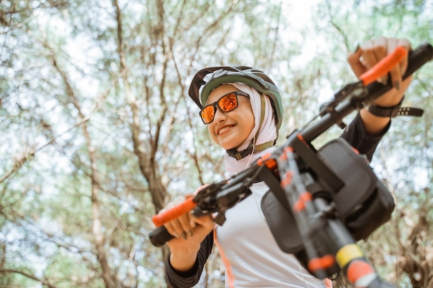 Atractiva chica con velo en gafas de sol sonriendo mientras anda en bicicleta en el parque