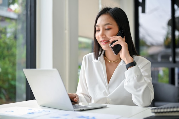 Atractiva empresaria asiática hablando por teléfono con su socio comercial