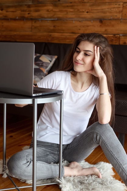 Atractiva estudiante feliz sonriente con video chat sentado en el suelo