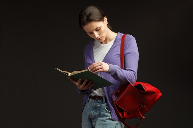 Atractiva estudiante de pie con mochila roja y libro de educación de lectura aislado