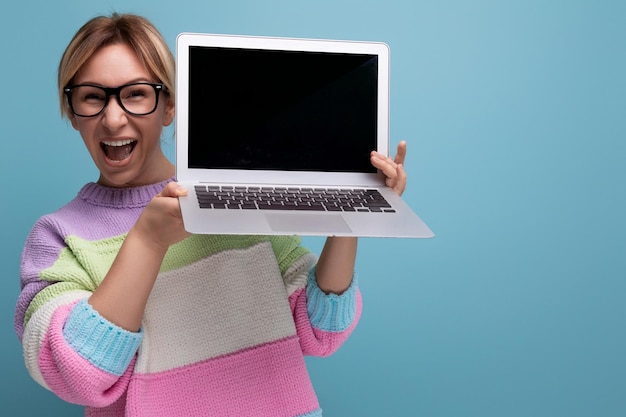 Atractiva y exitosa mujer independiente rubia con un suéter a rayas demuestra una maqueta de una computadora portátil