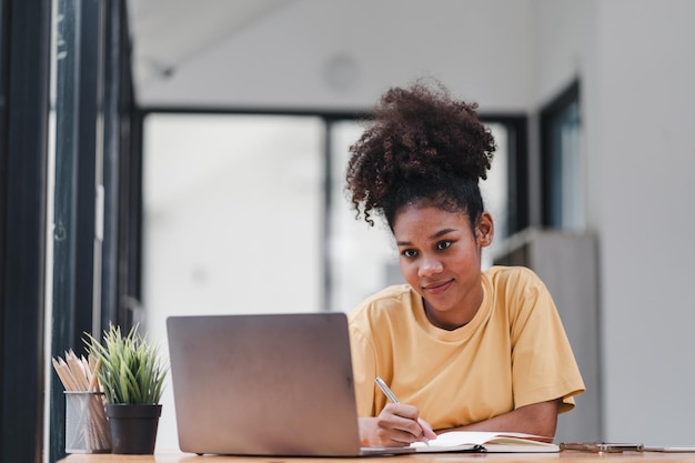 Una atractiva y feliz mujer de negocios del milenio está sentada en un sofá en su sala de estar trabajando con una computadora portátil en casa