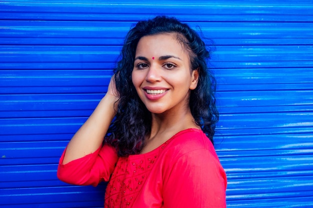 Foto atractiva hermosa feliz joven mujer hispana latina con bindi de teca en la frente sonriendo sobre fondo azul de wall street