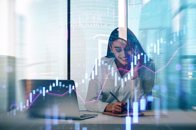 Atractiva jovem mulher de negócios europeia silhueta sentada em uma mesa com laptop em fundo borrado da cidade com gráfico forex sucesso finanças local de trabalho CEO e conceito futuro dupla exposição