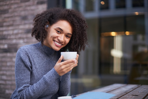 Atractiva joven afroamericana sosteniendo una taza de café aromático y sonriendo a la cámara