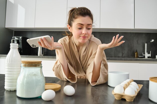 Atractiva joven alegre horneando en la cocina haciendo masa sosteniendo un libro de recetas con ideas