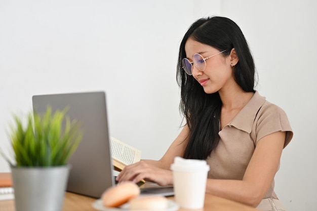 Atractiva joven asiática con gafas usando una computadora portátil