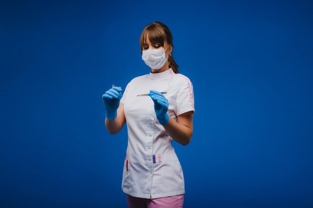 Una atractiva joven doctora sostiene un bisturí y mira directamente a la cámara. Concepto de salud, tratamiento y cirugía. Retrato de un médico sobre un fondo azul.