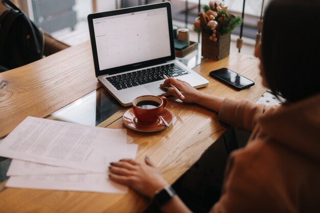 Atractiva joven empresaria está escribiendo en la computadora portátil y trabajando con documentos en papel