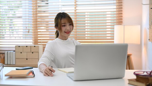 Atractiva joven empresaria con suéter blanco que trabaja desde casa con una computadora portátil