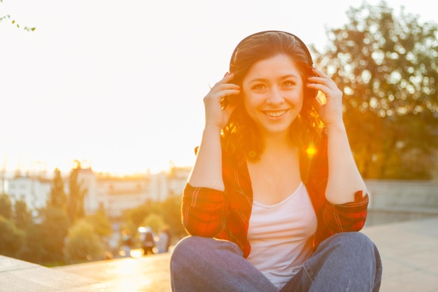 Atractiva joven estudiante escuchando música con auriculares al amanecer.