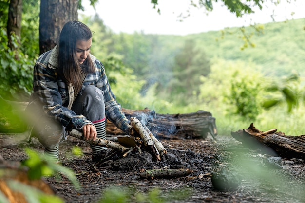 Una atractiva joven hace un fuego para mantenerse caliente en el bosque.