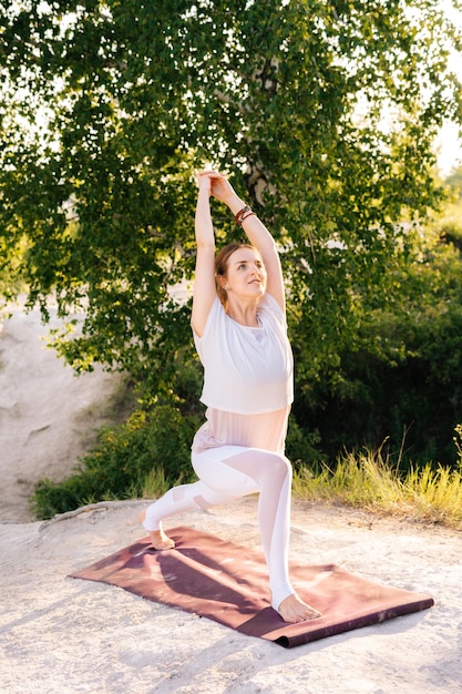 Atractiva joven haciendo una pose de asana de yoga guerrera sobre un fondo rocoso de un hermoso paisaje