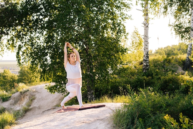 Atractiva joven haciendo una pose de asana de yoga guerrera sobre un fondo rocoso de un hermoso paisaje