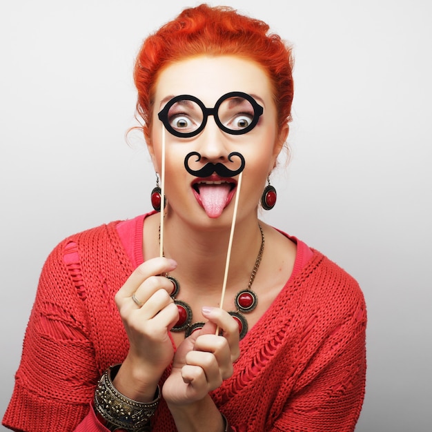 Atractiva joven juguetona con bigote y gafas en un palo. Listo para la fiesta.