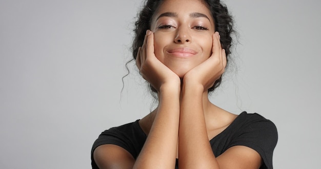 Foto atractiva joven modelo del medio oriente tocando su cara bonita con una piel impecable y sonriendo